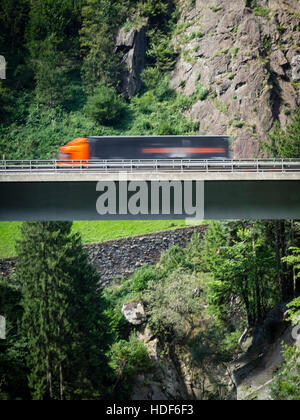 Ein verschwommener LKW fährt über eine Autobahn Brücke der Schweiz Autobahn A2 in Richtung Gotthard-Tunnel durch die Schweizer Alpen. Stockfoto