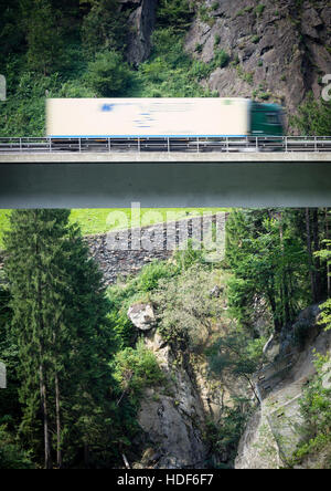 Ein verschwommener LKW fährt über eine Autobahn Brücke der Schweiz Autobahn A2 in Richtung Gotthard-Tunnel durch die Schweizer Alpen. Stockfoto