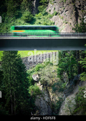 Ein verschwommener Coach fährt über eine Autobahn Brücke der Schweiz Autobahn A2 in Richtung Gotthard-Tunnel durch die Schweizer Alpen. Stockfoto