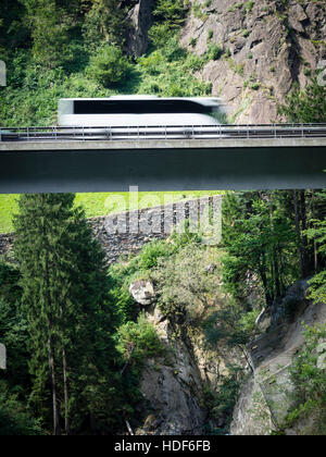 Ein verschwommener Coach fährt über eine Autobahn Brücke der Schweiz Autobahn A2 in Richtung Gotthard-Tunnel durch die Schweizer Alpen. Stockfoto