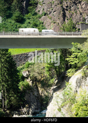 Eine verschwommene Karawane fährt über eine Autobahn Brücke der Schweiz Autobahn A2 in Richtung Gotthard-Tunnel durch die Schweizer Alpen. Stockfoto
