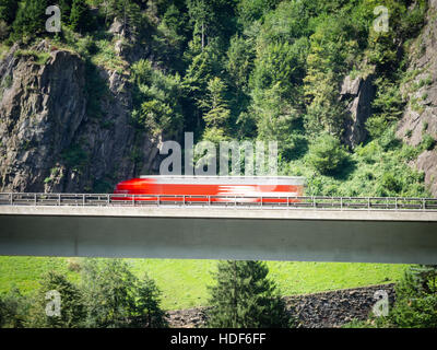 Ein verschwommener LKW fährt über eine Autobahn Brücke der Schweiz Autobahn A2 in Richtung Gotthard-Tunnel durch die Schweizer Alpen. Stockfoto