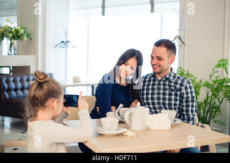 Familie, Elternschaft, Menschen Technologiekonzept - Nahaufnahme von glückliche Mutter, Vater und kleine Mädchen essen, Kind nehmen Foto per Smartphone im Restaurant Stockfoto