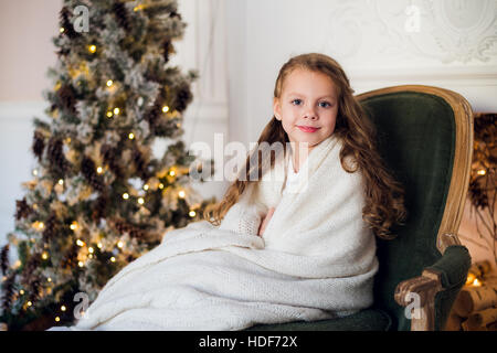 Niedliche kleine Mädchen sitzt durch den Weihnachtsbaum, eingehüllt in eine warme Decke zu Hause Stockfoto