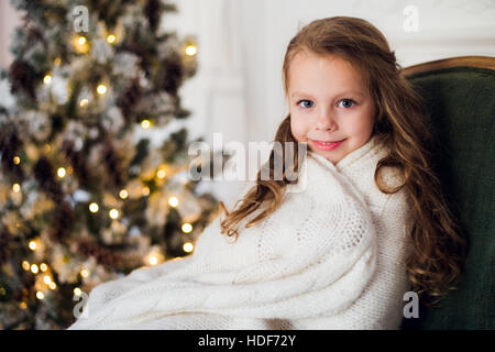 Niedliche kleine Mädchen sitzt durch den Weihnachtsbaum, eingehüllt in eine warme Decke zu Hause Stockfoto