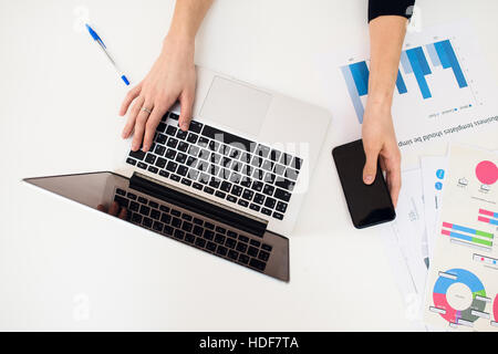 Laptop mit Frauen Hand und Papier Diagramm auf weißen Tisch. Stockfoto