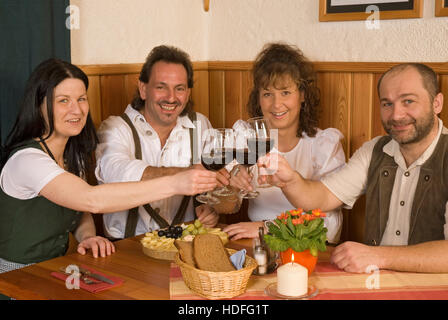 Zwei Paare gekleidet in traditionellen Kleidern sitzen an einem Tisch, klirrende Gläser Wein Stockfoto