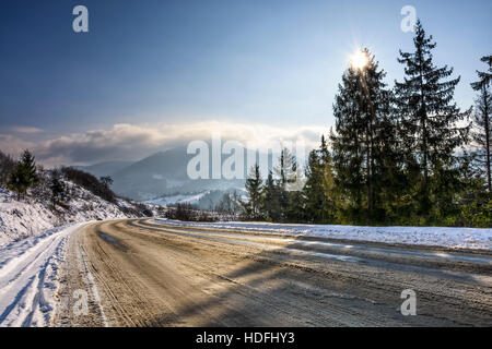 Winter-Berglandschaft. Straße führt hinab zum Dorf Throug Fichten-Wald auf frischen frostigen Tag mit Schnee bedeckt Stockfoto