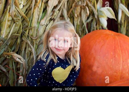 entzückende schulpflichtige Mädchen sitzen auf Bauernhof neben Riesenkürbis für fallen Herbstsaison Stockfoto