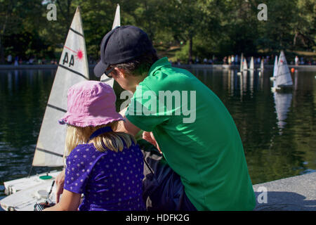 Vater und Tochter spielen mit Fernbedienung Segelboot im Central Park, Manhattan, New York City Stockfoto