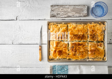 Griechischer Kuchen Spanakopita in der Metall-Pfanne mit Geschirr horizontale Stockfoto