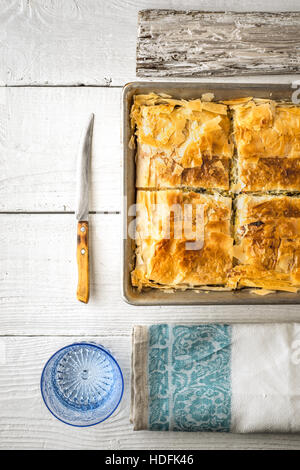 Griechischer Kuchen Spanakopita in der Metall-Pfanne mit vertikaler Tischwäsche Stockfoto