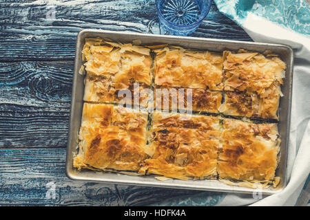 Griechischer Kuchen Spanakopita in der Metall-Pfanne auf der blauen hölzernen Tischplatte Ansicht Stockfoto