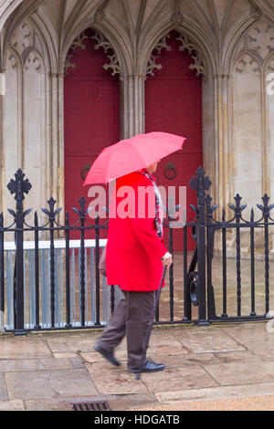 Winchester, Hampshire, UK 12. Dezember 2016. Lady eilt entlang Straße Vergangenheit Winchester Cathedral, die versuchen, zu halten unter roten Regenschirm an einem verregneten Tag regnerisch bei Winchester im Dezember trocken.  Bildnachweis: Carolyn Jenkins/Alamy Live-Nachrichten Stockfoto