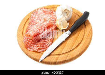 Geschnittene Salami auf Holzbrett mit Knoblauch und Messer isoliert auf weiß Stockfoto