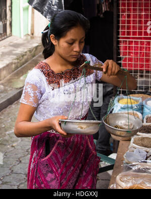 Eine attraktive junge Maya-Frau in traditioneller Kleidung verwendet einen Gleichgewicht Maßstab auf dem Markt von Santiago Atitlan, Guatemala. Stockfoto