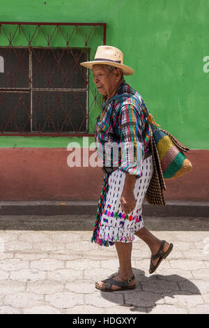 Ein älterer Maya-Mann in traditioneller Kleidung von San Pedro la Laguna, Guatemala, geht auf eine gepflasterte Straße vor einem Erdton bemalte Wand in tha Stockfoto