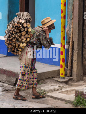 Ein Maya-armer in zerlumpten traditionelle Kleidung trägt eine schwere Last von Holz mit einem Tumpline in San Pedro la Laguna, Guatemala.  Hell lackiert blau Stockfoto
