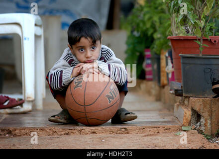 Ein syrischer Flüchtlingskind spielt mit einem Ball in eine Siedlung Camp, wo er unter einem Olivenhain im Koura, in der Nähe von Tripoli, Libanon lebt. Stockfoto