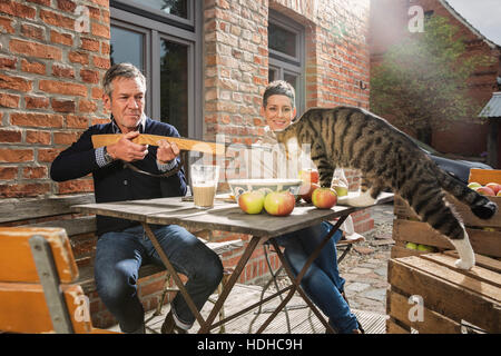 Spielerische Mann, mit dem Ziel Spielzeug Gewehr auf Tabby Katze sitzend mit Frau im Hinterhof Stockfoto