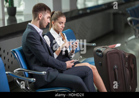 Junges Unternehmen-paar, die Benutzung von Mobiltelefonen während der Wartezeit am Flughafen Stockfoto