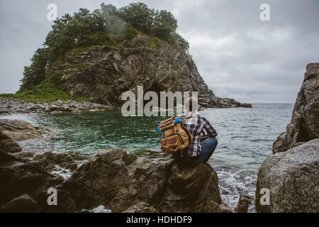 Rückansicht des Wanderer auf Felsformation am Strand gegen Himmel sitzen Stockfoto