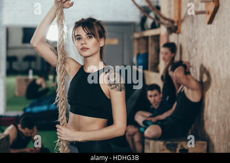 Porträt von zuversichtlich Sportlerin halten Seil stehend im Fitnessstudio mit Freunden im Hintergrund Stockfoto