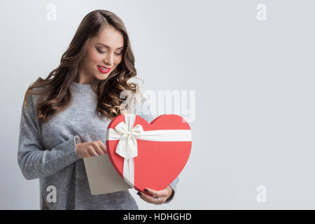 Junges Mädchen mit roten herzförmigen Geschenkbox auf weißem Hintergrund Stockfoto