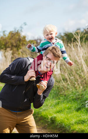 Ein Mann und ein kleiner Junge auf einem Spaziergang, ein Vater mit seinem Sohn eine Huckepack. Stockfoto