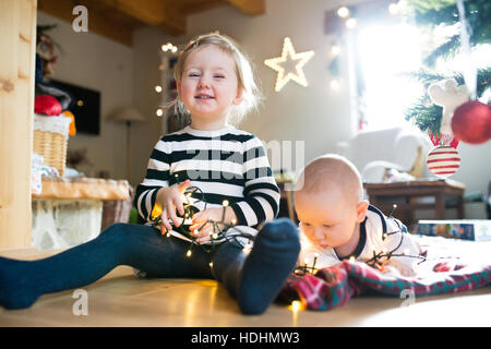 Jungen und Mädchen unter Weihnachtsbaum verstrickt in Lichterkette Stockfoto