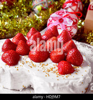 Nahaufnahme einer herzförmigen Kuchen mit Sahne und garniert mit Erdbeeren, auf einem Tisch voller Geschenke und Weihnachtsschmuck Stockfoto