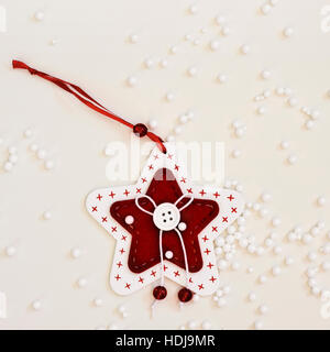 High-Angle Shot von einer gemütlichen handgefertigten Christbaumschmuck platziert auf einer Off-White Oberfläche gesprenkelt mit kleinen Plastikbällen Schnee simulieren Stockfoto