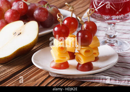 Rote Trauben und Käse am Spieß und einem Glas Wein hautnah auf einem Teller. horizontale Stockfoto