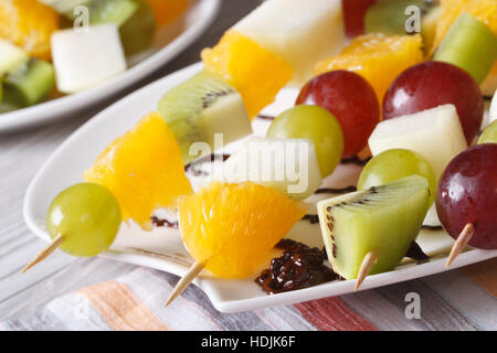 Frisches Obst Orangen, Kiwi, Trauben und Birnen auf Spieße auf einem Teller-Makro. horizontale Stockfoto