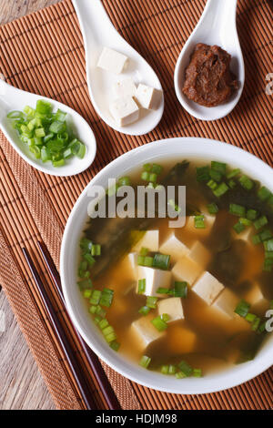 Japanische Miso-Suppe in einer weißen Schüssel und Zutaten in einem Löffel auf eine Tabelle Nahaufnahme. vertikale Ansicht von oben Stockfoto