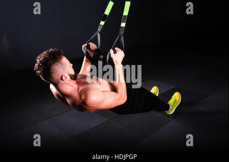 Einen schöner junger tapferer lockiger bärtiger bemuskelt Mann mit einem Bart macht Gesamtwiderstand Übungen Fitness Trx Bändern trainieren Sie im Fitness-Studio Stockfoto