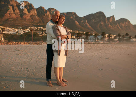 Voller Länge Schuss von romantischen älteres paar umarmt am Ufer Meeres.  Senior Liebespaar Aussicht auf den Sonnenuntergang am Strand genießen. Stockfoto