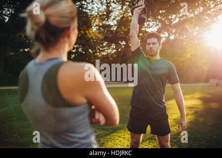 Gesunden jungen Mann mit weiblichen Trainer Training mit Kettlebell in den Park. Passen Sie Mann mit weiblichen Trainer vor Ausübung. Stockfoto