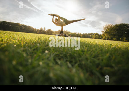 Passen Sie junges Paar Acroyoga auf Rasen zu tun. Mann und Frau im Park paar Yoga-Übungen praktizieren. Stockfoto