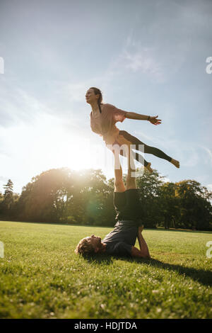 Vertikale Aufnahme des Fit junges Paar akrobatische Yoga zu tun. Mann auf dem Rasen liegen und balancing Frau in seinen Füßen im Park. Stockfoto