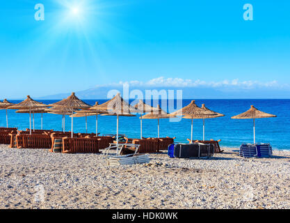 Sommer morgen kiesiger Strand mit liegen und Sonnenschirm strohig (Borsh, Albanien). Stockfoto