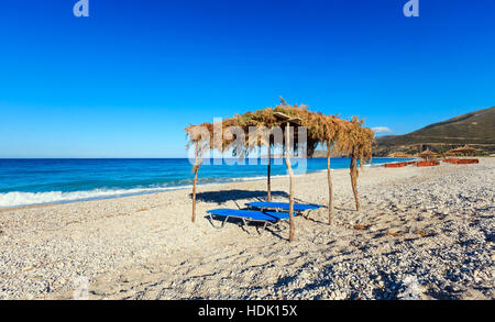 Sommer morgen kiesiger Strand mit Sonnenliegen und Baldachin (Borsh, Albanien). Stockfoto