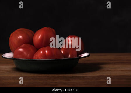 Reife, rote Tomaten auf dem Teller auf dunklem Hintergrund Stockfoto