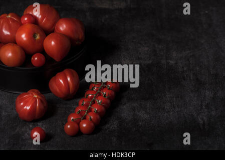 Reife, rote Tomaten auf dem Teller auf dem Tisch, auf einem dunklen Hintergrund Stockfoto