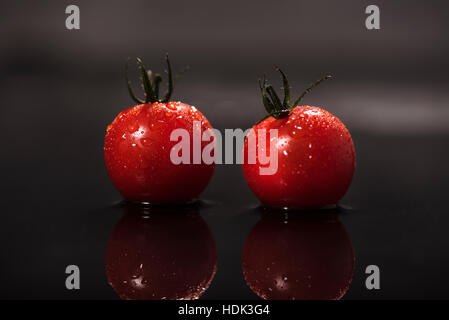 Zwei Reife, rote Tomaten mit Tropfen Wasser auf dem Tisch, dunklen Hintergrund abprallen Stockfoto