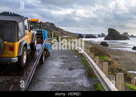 Meyers Beach, Oregon - 27 Oktober: Flachbett Abschleppwagen eine defekte Fahrzeug mit einer schönen Küstenlandschaft im Hintergrund laden. 27. Oktober 2016, Stockfoto