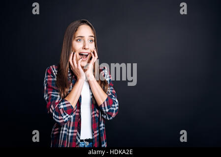 Emotionale junge Frau steht auf schwarzem Hintergrund Stockfoto