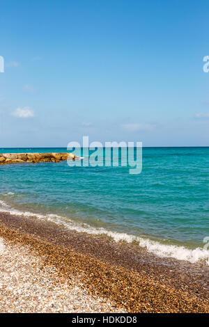 Ufer des Strandes mit Steinen und Steg im Hintergrund. Vertikales Bild. Stockfoto