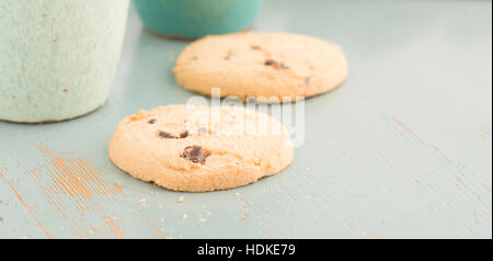 Chocolate Chip Cookies und Kaffee oder Tee Tassen. Süße Speisen, Nachtisch oder Snack. Die Cookies werden auf einem Küchentisch serviert. Stockfoto