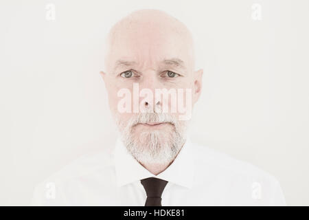Greis, Blick in die Kamera. Ernsthafte und entschlossene Gesichtsausdruck. Er trägt formelle Kleidung und Stand vor der weißen Wand. Stockfoto